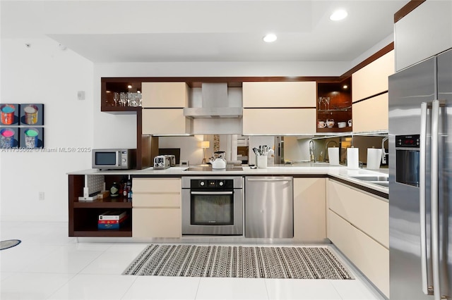 kitchen featuring light tile patterned flooring, sink, appliances with stainless steel finishes, cream cabinets, and wall chimney range hood