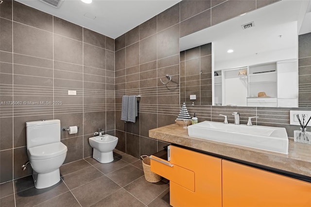 bathroom with tile walls, vanity, toilet, a bidet, and tile patterned floors