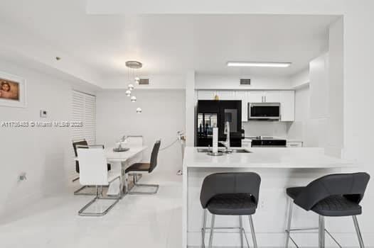 kitchen with sink, white cabinetry, fridge, a kitchen breakfast bar, and kitchen peninsula