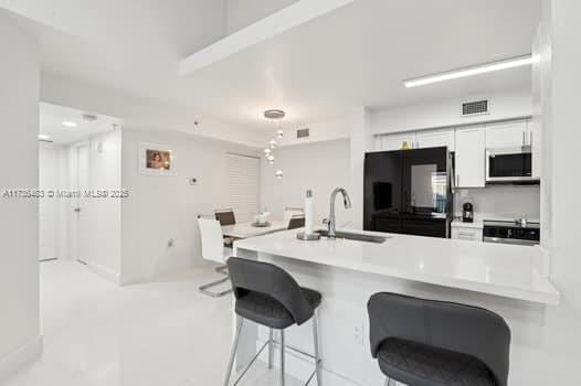 kitchen featuring sink, a breakfast bar area, white cabinetry, black fridge, and kitchen peninsula