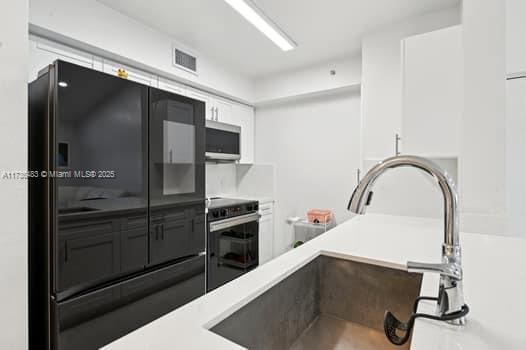 kitchen with black fridge, sink, white cabinets, and electric range