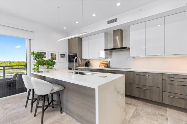 kitchen with wall chimney range hood, sink, a breakfast bar, white cabinetry, and black electric stovetop