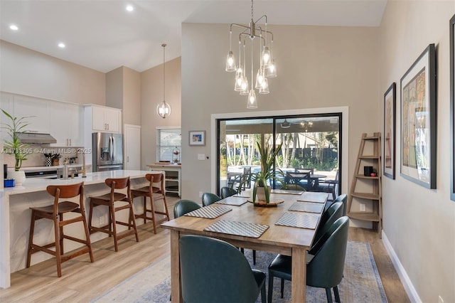 dining area featuring a notable chandelier, high vaulted ceiling, and light wood-type flooring