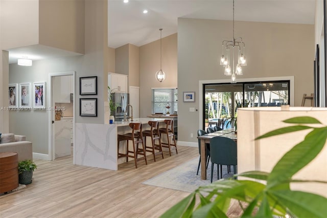 kitchen featuring light hardwood / wood-style flooring, white cabinetry, high vaulted ceiling, a kitchen bar, and decorative light fixtures