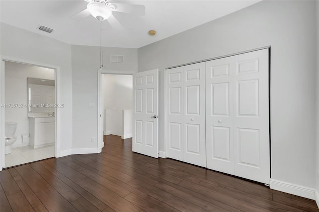 unfurnished bedroom featuring dark wood-type flooring, a closet, ceiling fan, and ensuite bathroom