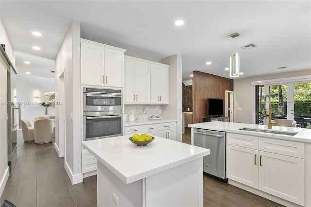 kitchen with appliances with stainless steel finishes, pendant lighting, tasteful backsplash, white cabinetry, and a center island