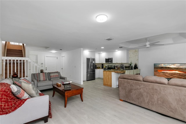 living room with ceiling fan, a tray ceiling, and light wood-type flooring