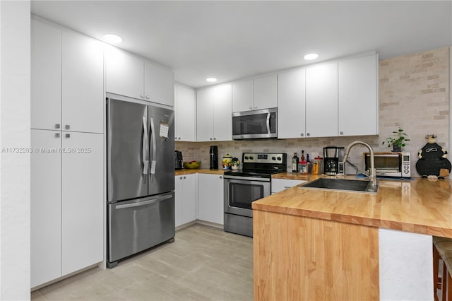 kitchen featuring butcher block counters, sink, appliances with stainless steel finishes, decorative backsplash, and white cabinets