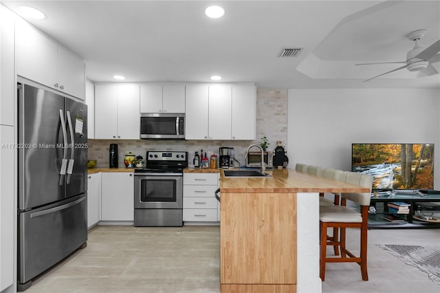 kitchen with sink, a breakfast bar, appliances with stainless steel finishes, white cabinetry, and kitchen peninsula