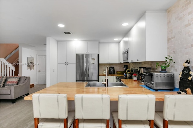 kitchen with a breakfast bar, sink, appliances with stainless steel finishes, decorative backsplash, and white cabinets