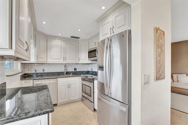 kitchen featuring appliances with stainless steel finishes, sink, white cabinets, backsplash, and dark stone counters