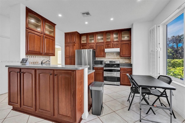 kitchen featuring decorative backsplash, light tile patterned flooring, kitchen peninsula, and appliances with stainless steel finishes