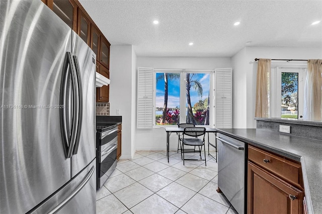 kitchen with stainless steel appliances, light tile patterned flooring, backsplash, and a textured ceiling