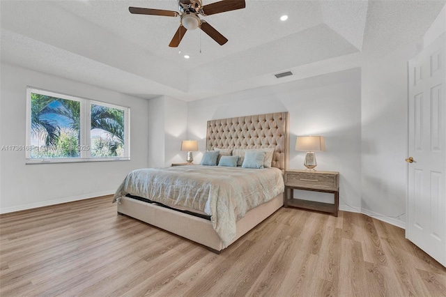 bedroom featuring a raised ceiling, a textured ceiling, and light wood-type flooring