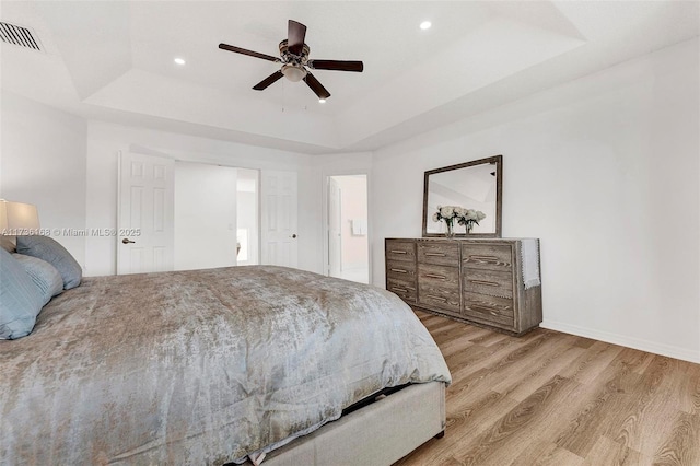 bedroom featuring ceiling fan, light wood-type flooring, and a tray ceiling