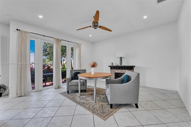 sitting room with a stone fireplace, light tile patterned floors, a textured ceiling, and ceiling fan