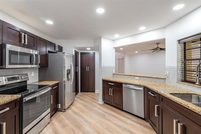 kitchen featuring sink, appliances with stainless steel finishes, light stone counters, light hardwood / wood-style floors, and kitchen peninsula