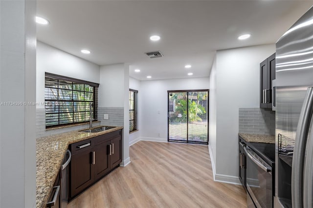 kitchen with appliances with stainless steel finishes, sink, light stone counters, plenty of natural light, and light hardwood / wood-style flooring