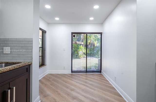 interior space with dark brown cabinetry, sink, tasteful backsplash, light wood-type flooring, and dark stone countertops