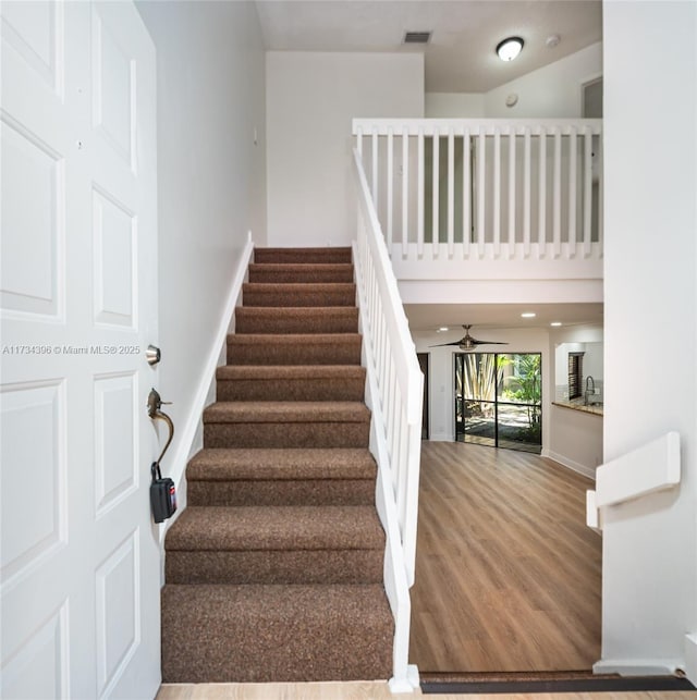 stairway with ceiling fan, wood-type flooring, sink, and a high ceiling