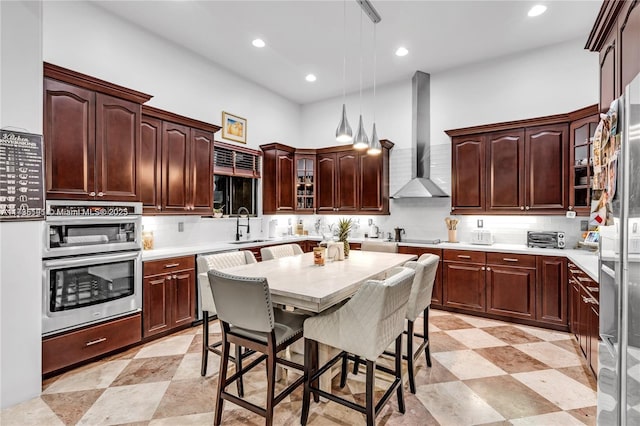 kitchen with tasteful backsplash, a breakfast bar area, dishwashing machine, hanging light fixtures, and wall chimney range hood