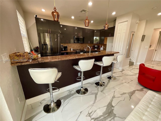 kitchen featuring stainless steel appliances, decorative light fixtures, kitchen peninsula, and a breakfast bar area