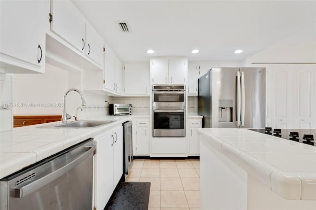 kitchen featuring sink, appliances with stainless steel finishes, white cabinets, light tile patterned flooring, and tile countertops