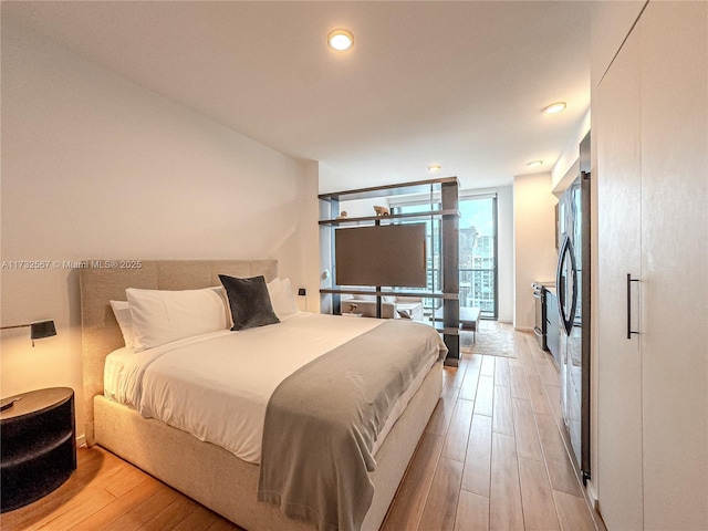 bedroom featuring expansive windows, fridge, and light wood-type flooring