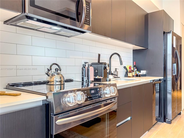 kitchen with tasteful backsplash, stainless steel appliances, light hardwood / wood-style floors, and sink