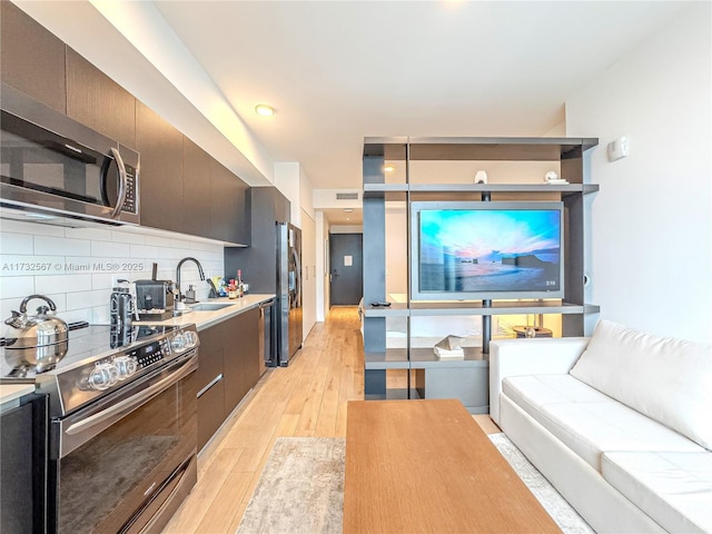 kitchen with tasteful backsplash, appliances with stainless steel finishes, light hardwood / wood-style floors, and sink