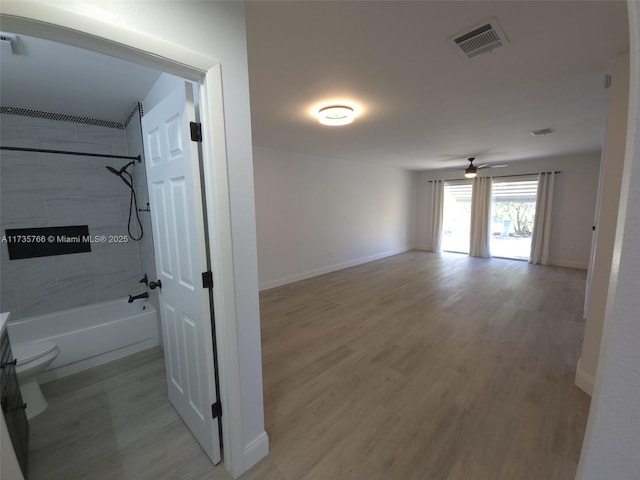 interior space featuring tiled shower / bath combo, hardwood / wood-style floors, ceiling fan, and toilet