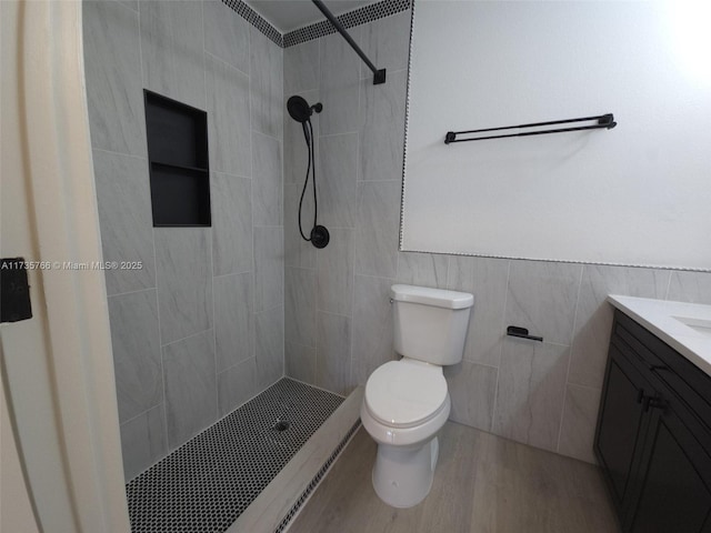 bathroom with tiled shower, toilet, wood-type flooring, tile walls, and vanity