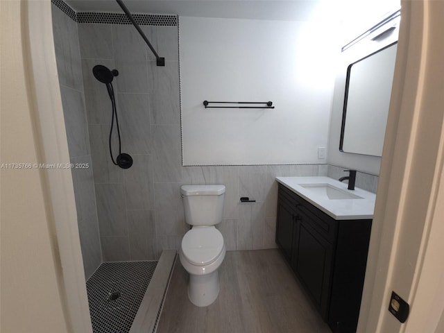 bathroom with tile walls, tiled shower, vanity, wood-type flooring, and toilet