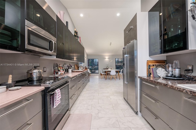 kitchen with stainless steel appliances, vaulted ceiling, and dark stone counters