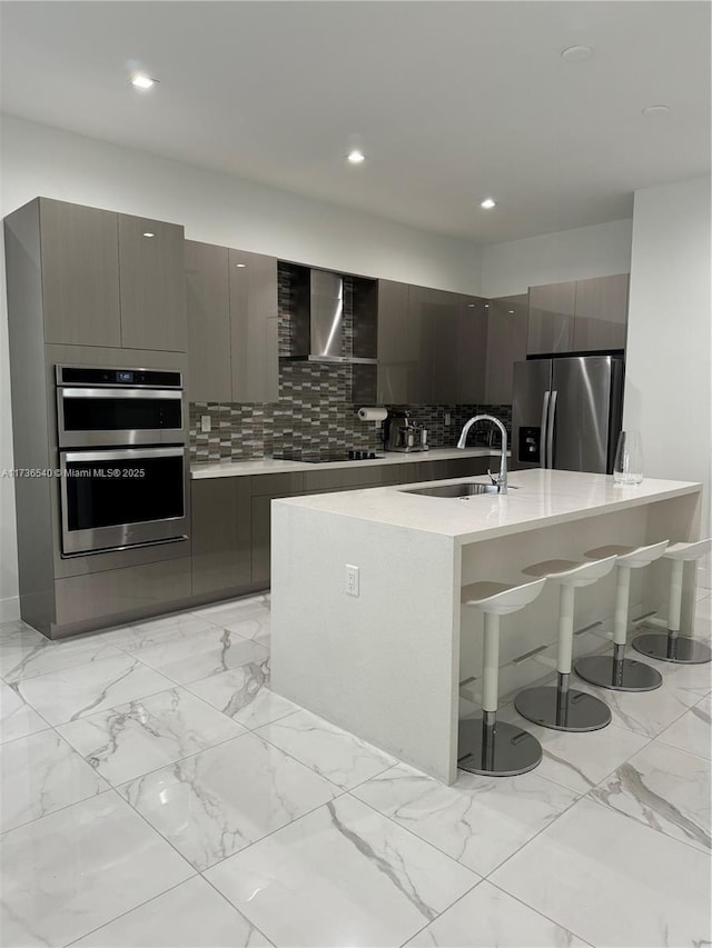 kitchen with stainless steel appliances, tasteful backsplash, sink, and wall chimney range hood