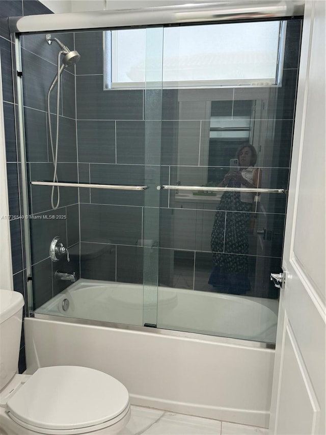 bathroom featuring toilet and bath / shower combo with glass door