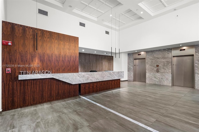 interior space with a towering ceiling, coffered ceiling, and elevator