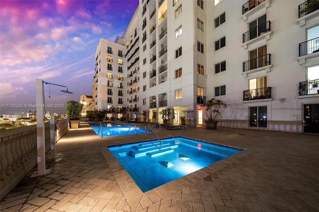 pool at dusk with a patio and a jacuzzi