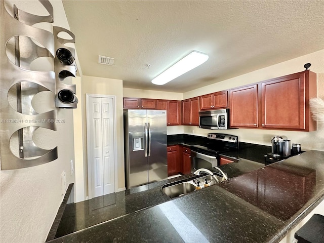 kitchen with appliances with stainless steel finishes, kitchen peninsula, sink, and a textured ceiling