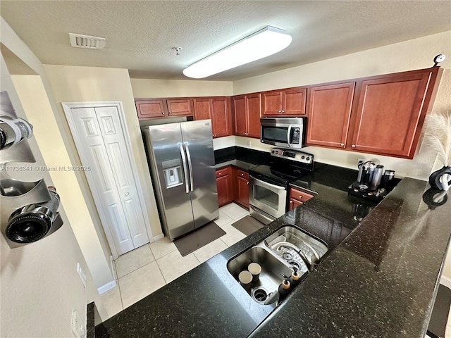 kitchen featuring light tile patterned floors, stainless steel appliances, a textured ceiling, kitchen peninsula, and dark stone counters