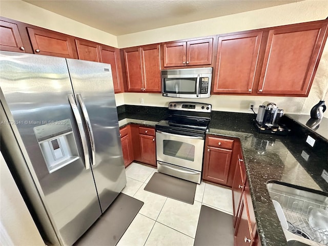 kitchen with dark stone countertops, light tile patterned floors, and stainless steel appliances