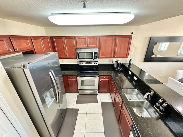 kitchen featuring stainless steel appliances, sink, light tile patterned floors, and dark stone counters