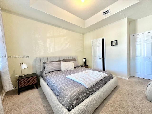 carpeted bedroom with a tray ceiling and a closet