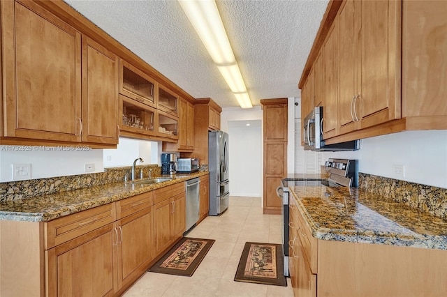 kitchen featuring brown cabinets, dark stone counters, stainless steel appliances, and a sink