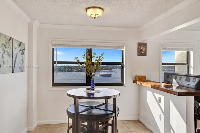 dining space featuring a water view, light tile patterned floors, crown molding, and a textured ceiling