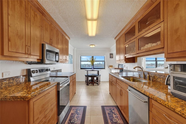 kitchen featuring light tile patterned floors, glass insert cabinets, stainless steel appliances, stone counters, and a sink