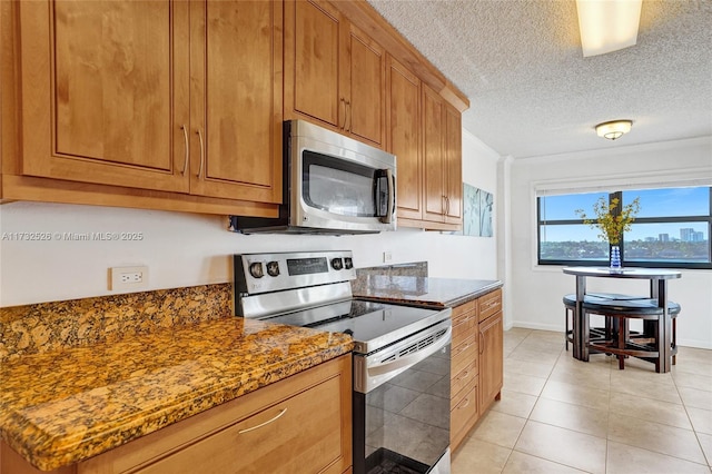 kitchen with brown cabinets, a textured ceiling, stainless steel appliances, and dark stone countertops