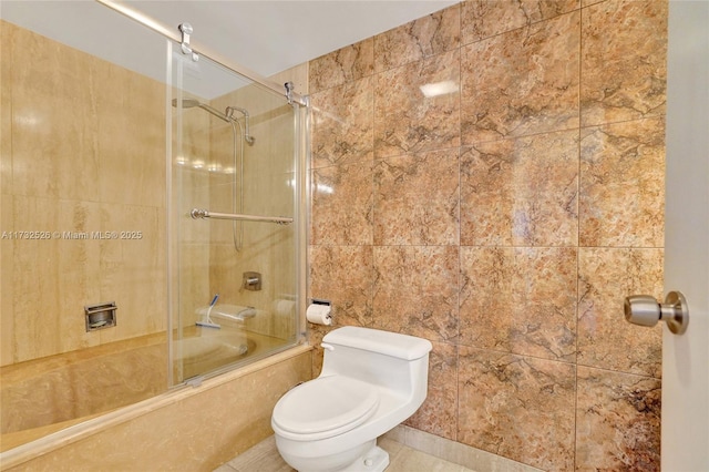 full bath with tile patterned flooring, tile walls, toilet, and bath / shower combo with glass door