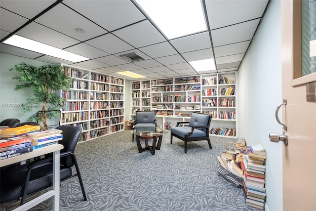 sitting room with wall of books, visible vents, and carpet flooring