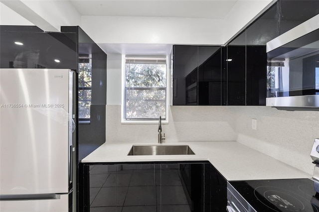 kitchen featuring dark cabinets, stainless steel appliances, a sink, light countertops, and backsplash